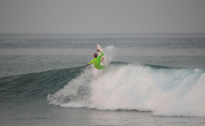 Uomo che surfa un'onda con una muta Xcel Comp verde lime fluo