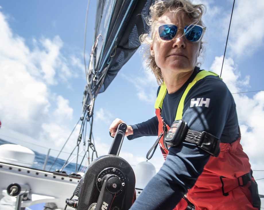 Woman sailor in mirrored sunglasses, navy Helly Hansen top and red salopettes working a winch