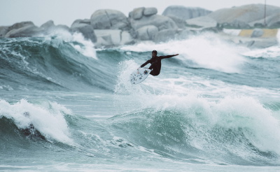 Surfista con muta invernale e cappuccio che entra in acqua fredda