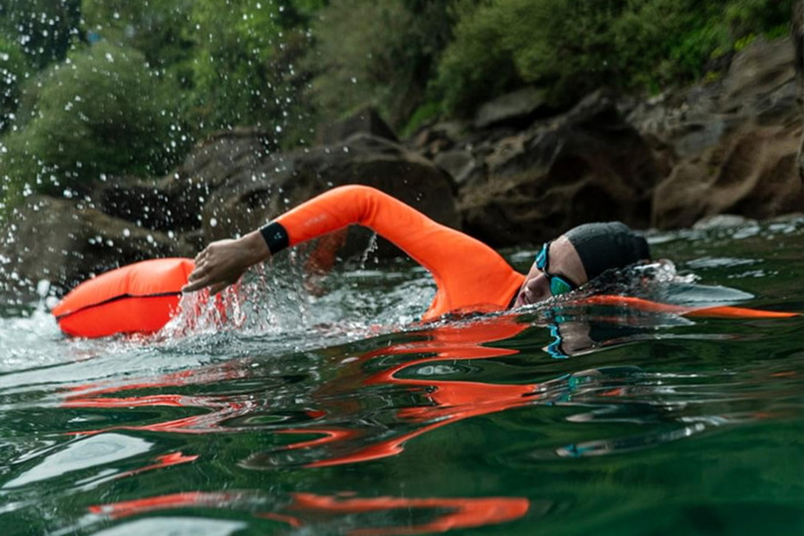 Open water swimmer in a wetsuit with hi-vis orange sleeves doing front crawl behind an orange tow float
