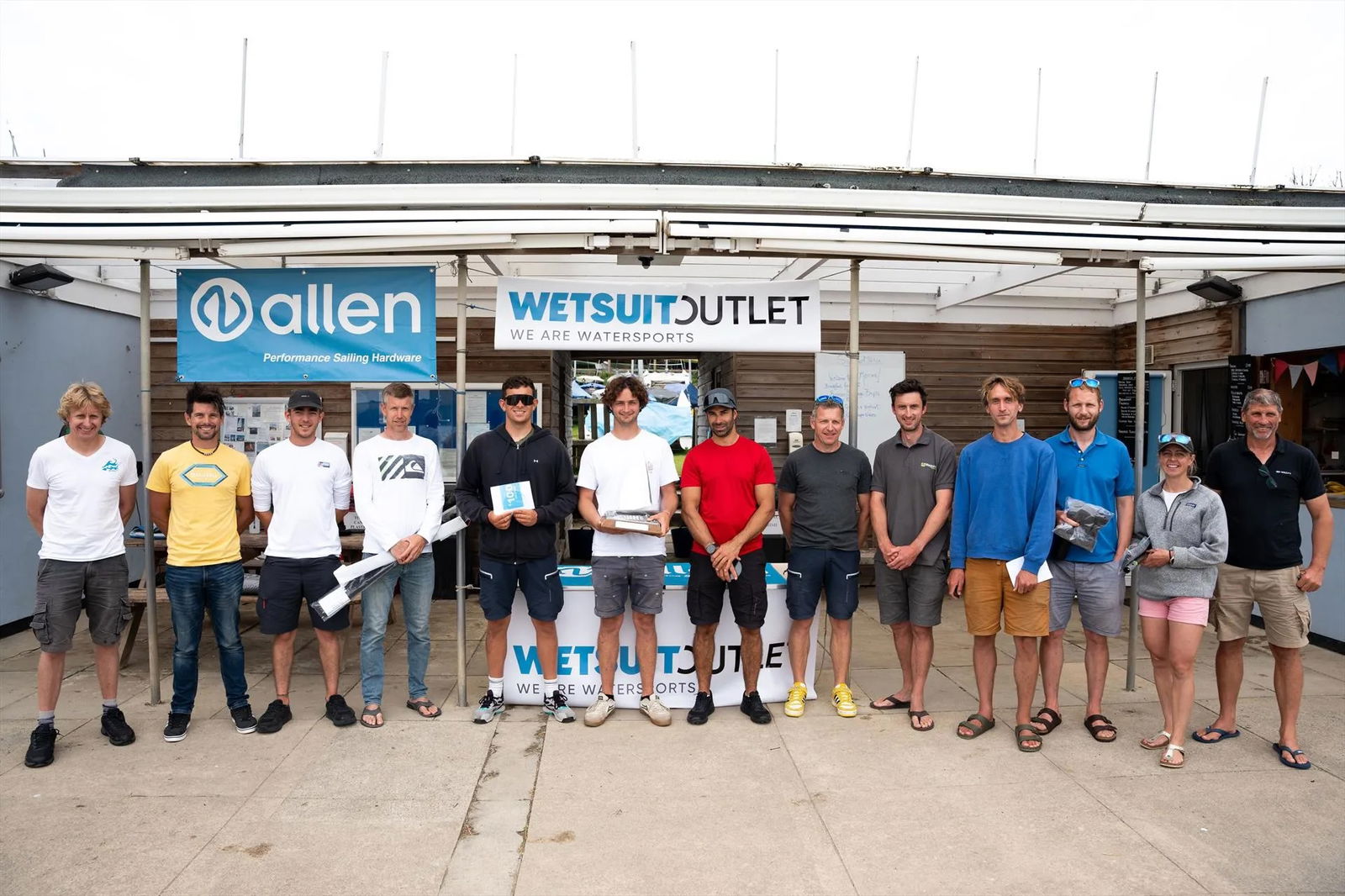 Line-up of prizewinning sailors under Allen and Wetsuit Outlet banners at the sailing club