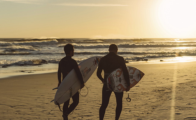 Surfer in Neoprenanzügen als Silhouette vor einem Sonnenuntergang