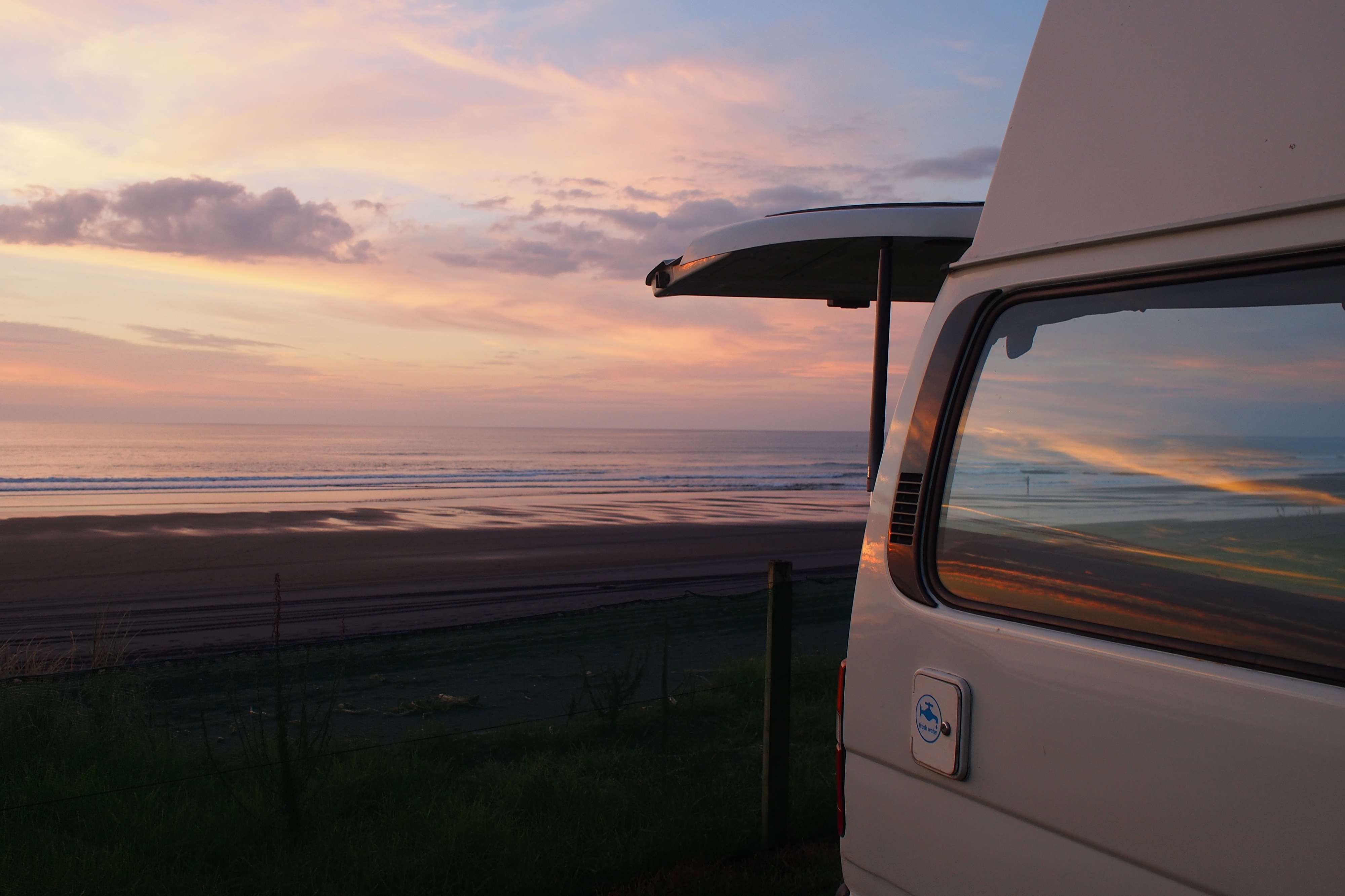 Campervan parked above a wide beach at sunset, side window open to the view