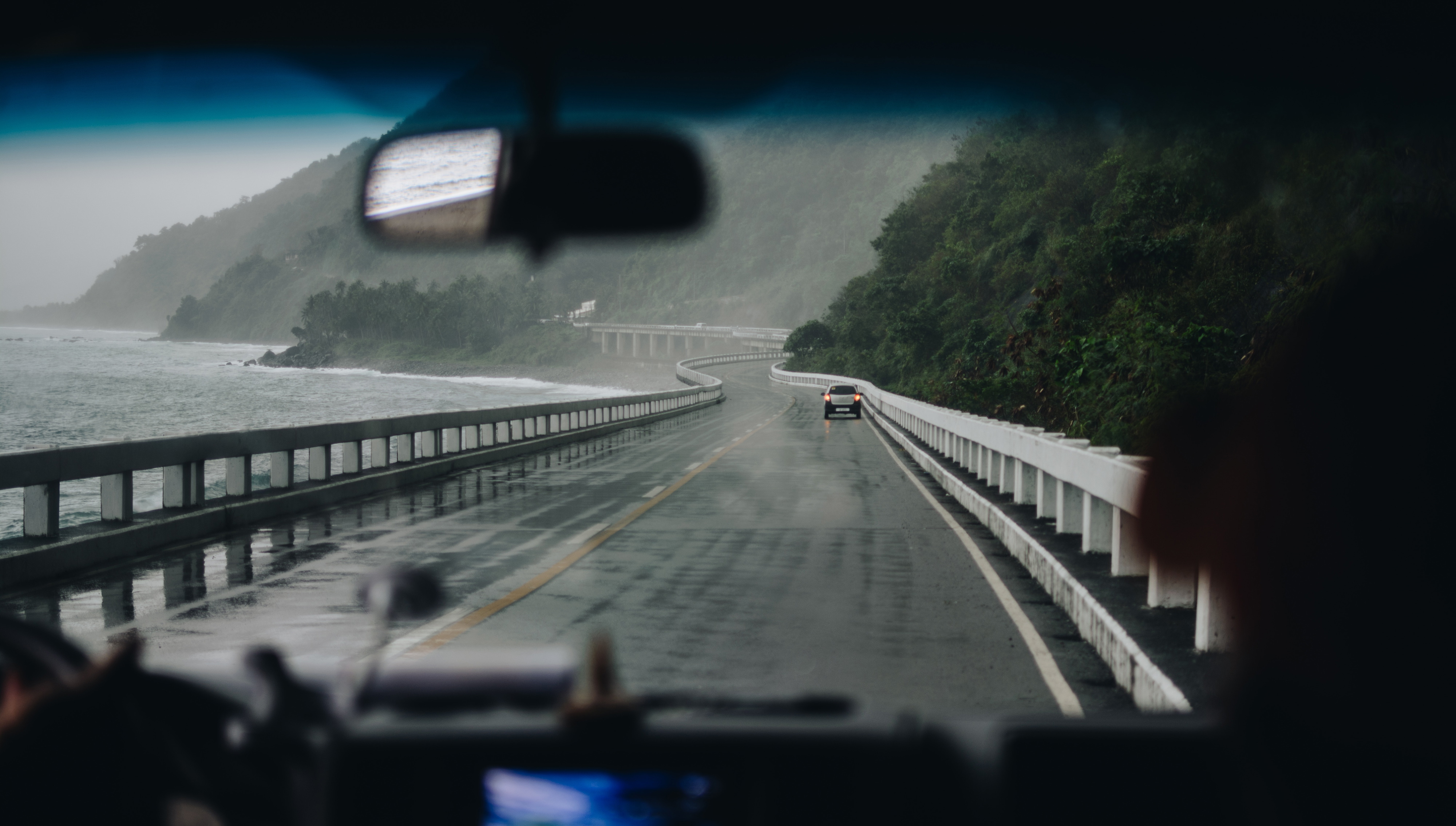 View through a car windscreen of an empty coastal road winding along a wooded shoreline