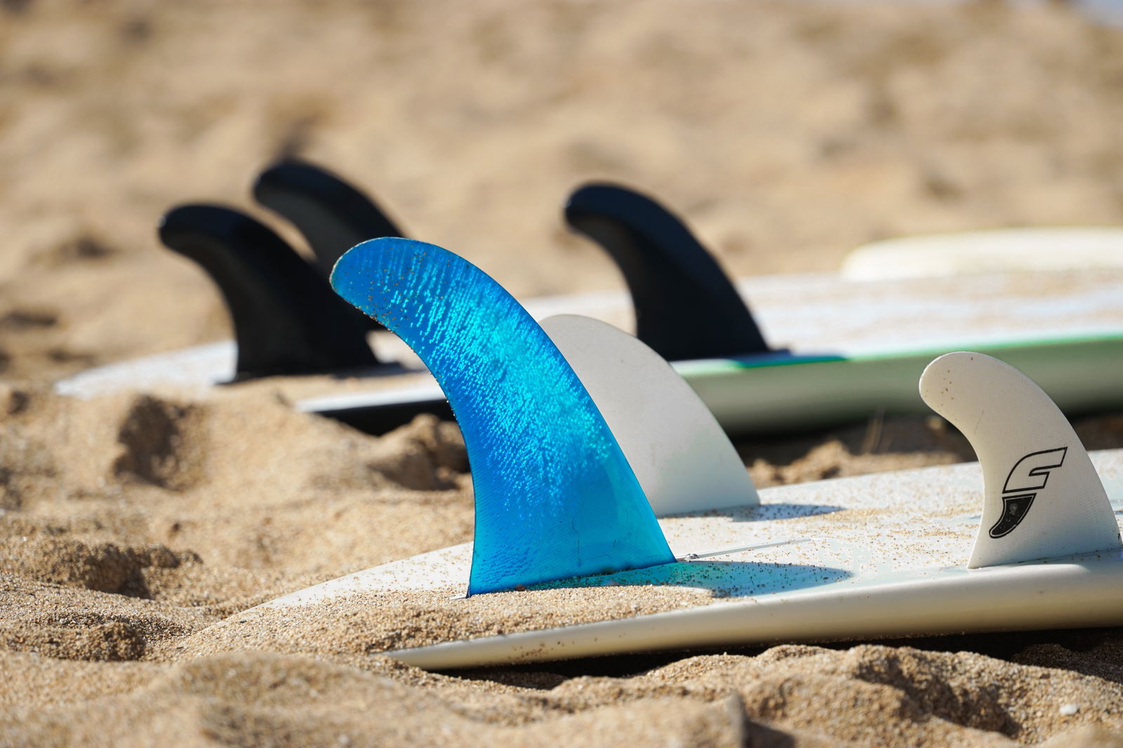 Surfboards resting fins up on the sand, a bright blue fin sharp in the foreground