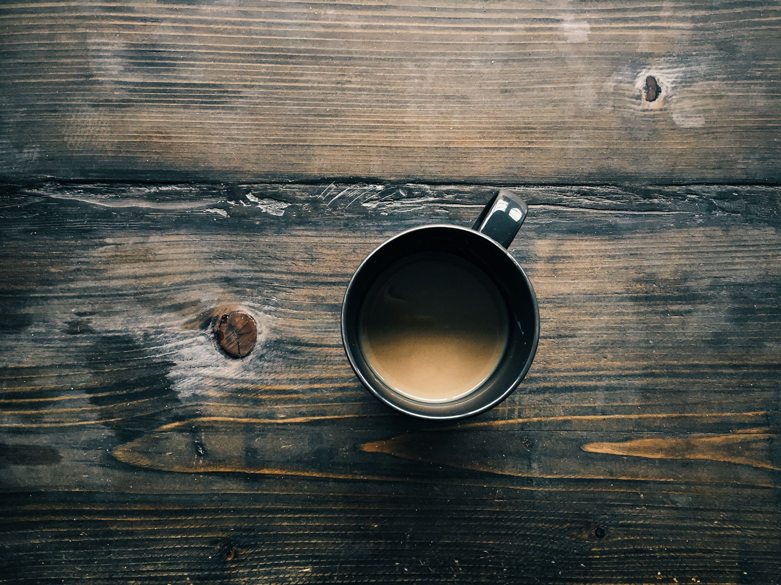 Overhead shot of a mug of milky coffee on weathered wooden decking